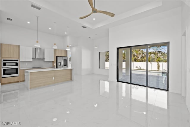 kitchen featuring wall chimney exhaust hood, stainless steel appliances, ceiling fan, sink, and white cabinetry