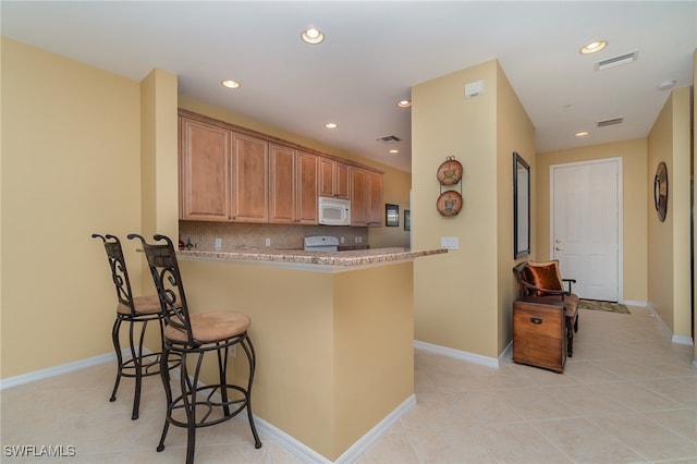 kitchen featuring a kitchen breakfast bar, light stone counters, backsplash, kitchen peninsula, and light tile patterned floors