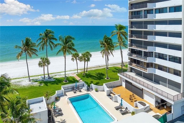 view of swimming pool with a patio area, a water view, and a beach view