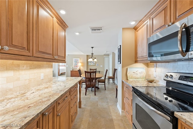 kitchen featuring backsplash, decorative light fixtures, light stone countertops, and stainless steel appliances