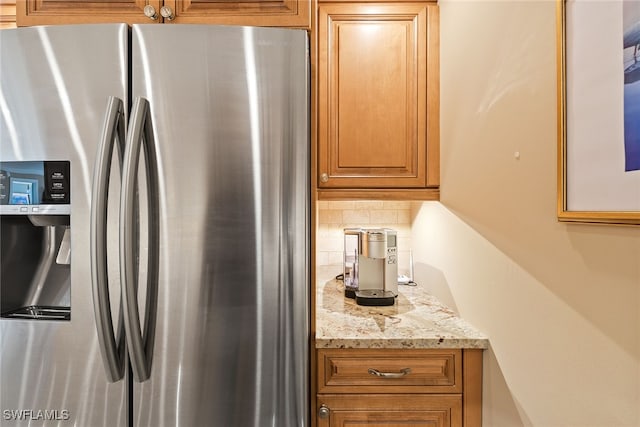 kitchen featuring decorative backsplash, stainless steel fridge, and light stone countertops