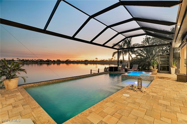 pool at dusk with glass enclosure, a patio area, a water view, and an in ground hot tub