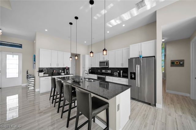 kitchen with white cabinetry, sink, dark stone counters, a center island with sink, and appliances with stainless steel finishes