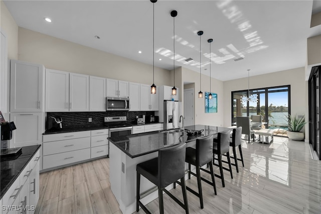 kitchen with appliances with stainless steel finishes, backsplash, a breakfast bar, a center island with sink, and white cabinets