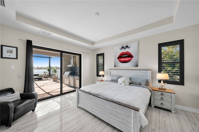 bedroom featuring access to exterior, a tray ceiling, and light hardwood / wood-style flooring