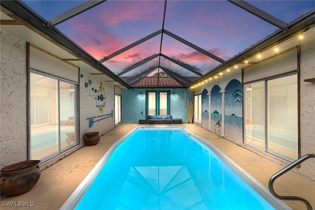 pool at dusk featuring glass enclosure and a patio area