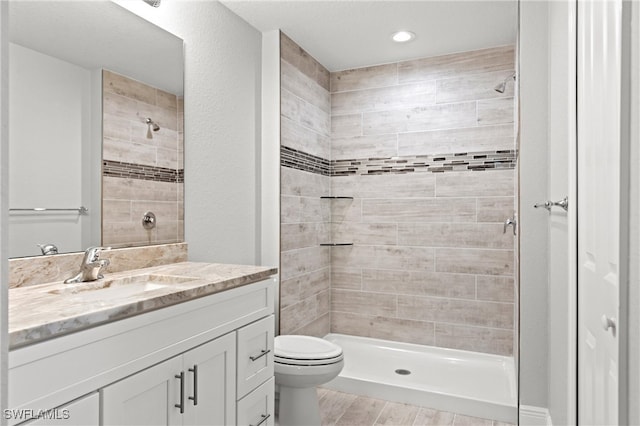 bathroom featuring toilet, hardwood / wood-style floors, vanity, and a tile shower