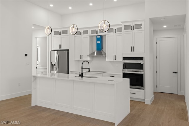 kitchen featuring wall chimney exhaust hood, appliances with stainless steel finishes, light wood-type flooring, and a sink