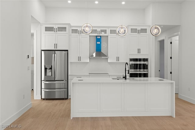 kitchen with light wood-style flooring, a kitchen island with sink, stainless steel appliances, a sink, and wall chimney exhaust hood