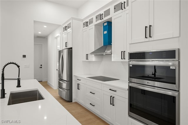 kitchen featuring stainless steel appliances, white cabinets, a sink, and wall chimney exhaust hood