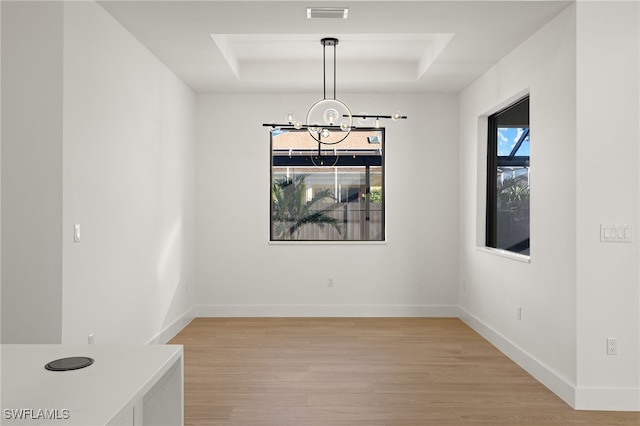 unfurnished dining area featuring visible vents, a raised ceiling, baseboards, light wood-style flooring, and a notable chandelier