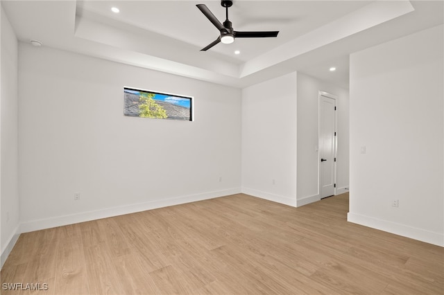 spare room with ceiling fan, a tray ceiling, light wood-type flooring, and baseboards