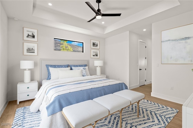 bedroom with recessed lighting, light wood-type flooring, a raised ceiling, and baseboards