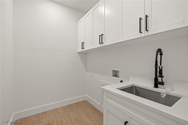 laundry area featuring hookup for a washing machine, cabinet space, light wood-style flooring, a sink, and baseboards