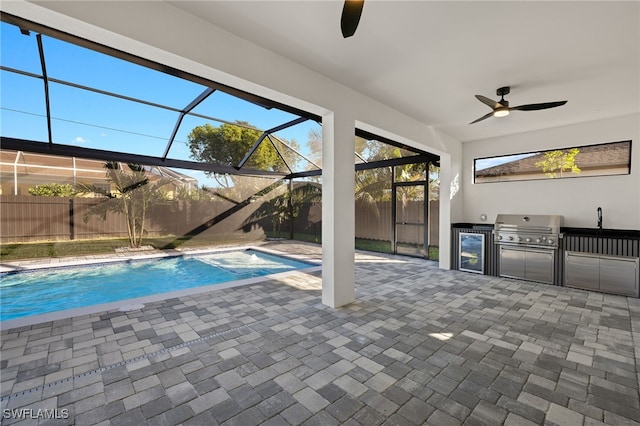 view of pool with a patio, glass enclosure, grilling area, fence, and exterior kitchen