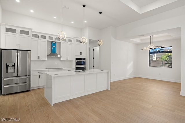 kitchen featuring wall chimney range hood, appliances with stainless steel finishes, a raised ceiling, and light countertops