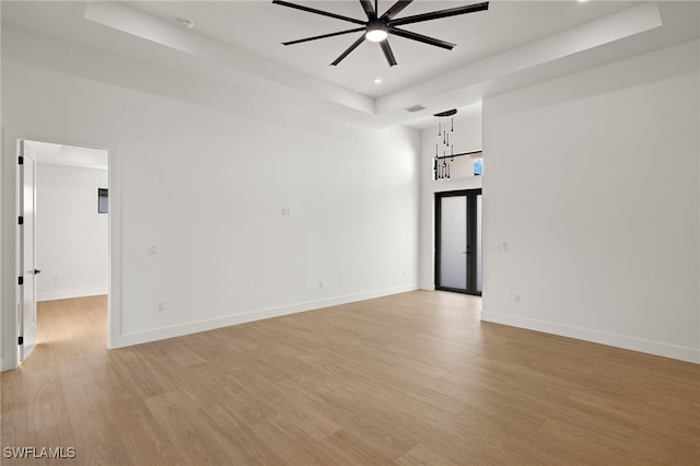 empty room with recessed lighting, light wood-type flooring, a raised ceiling, and baseboards