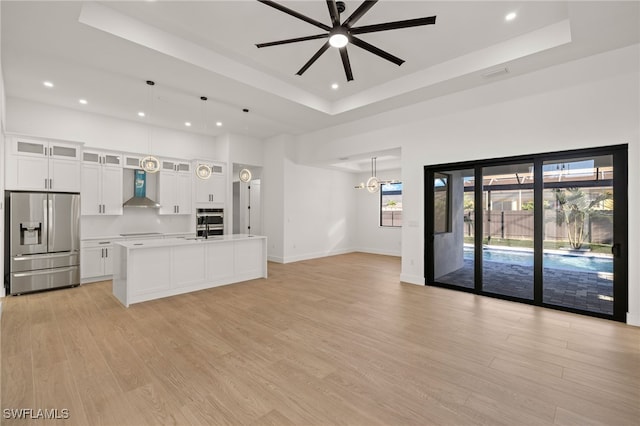 kitchen featuring open floor plan, light wood-type flooring, wall chimney exhaust hood, stainless steel fridge, and a raised ceiling