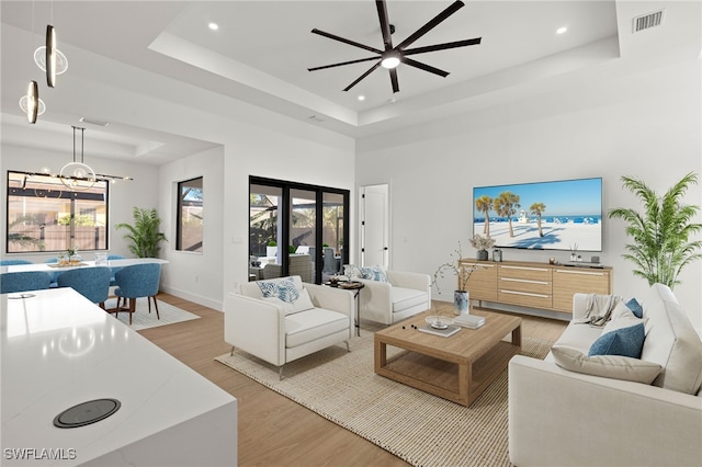 living room with a wealth of natural light, a tray ceiling, visible vents, and light wood-style flooring