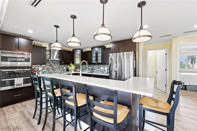 kitchen with a large island with sink, stainless steel appliances, dark brown cabinets, and light hardwood / wood-style floors