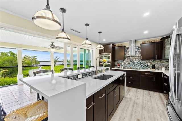 kitchen featuring tasteful backsplash, wall chimney exhaust hood, a kitchen island with sink, sink, and pendant lighting