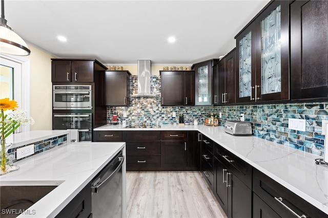 kitchen featuring backsplash, light hardwood / wood-style flooring, hanging light fixtures, and wall chimney range hood