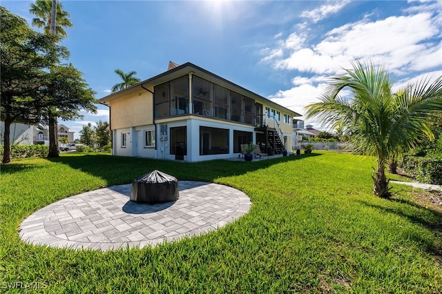 back of property with a patio area, an outdoor fire pit, a lawn, and a sunroom