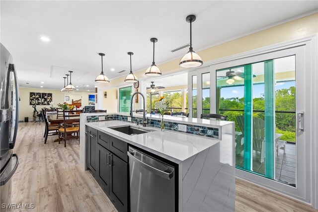 kitchen featuring a large island, sink, stainless steel appliances, decorative light fixtures, and light wood-type flooring