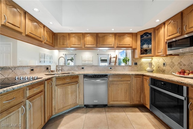 kitchen featuring sink, light stone counters, kitchen peninsula, light tile patterned flooring, and appliances with stainless steel finishes