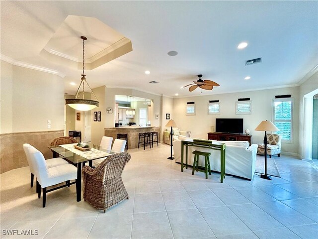 tiled dining area with ornamental molding, ceiling fan, and a tray ceiling