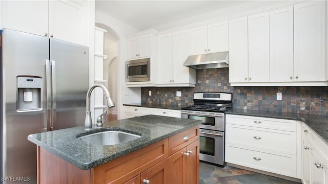 kitchen with sink, stainless steel appliances, dark stone countertops, a kitchen island with sink, and white cabinets