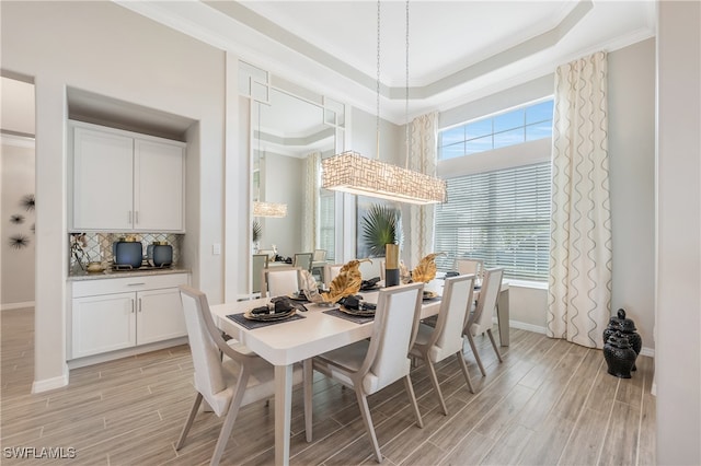 dining room featuring light hardwood / wood-style flooring, a raised ceiling, and ornamental molding