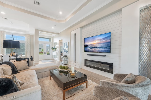 living room featuring ornamental molding, a fireplace, a tray ceiling, and light hardwood / wood-style flooring