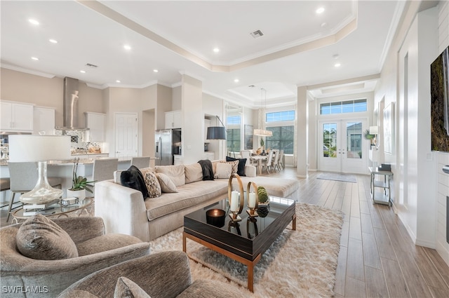 living room with french doors, light wood-type flooring, a raised ceiling, and crown molding