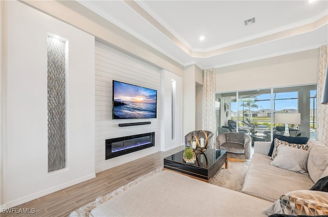 living room with a large fireplace, a raised ceiling, wood-type flooring, and crown molding