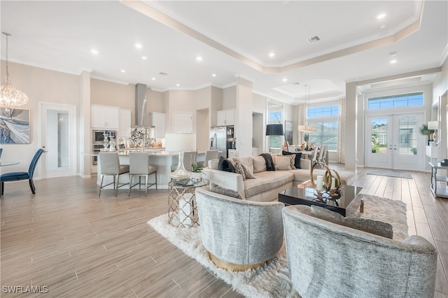 living room with french doors, light wood-type flooring, ornamental molding, a tray ceiling, and an inviting chandelier