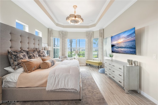 bedroom featuring a raised ceiling, light wood-type flooring, ornamental molding, and an inviting chandelier