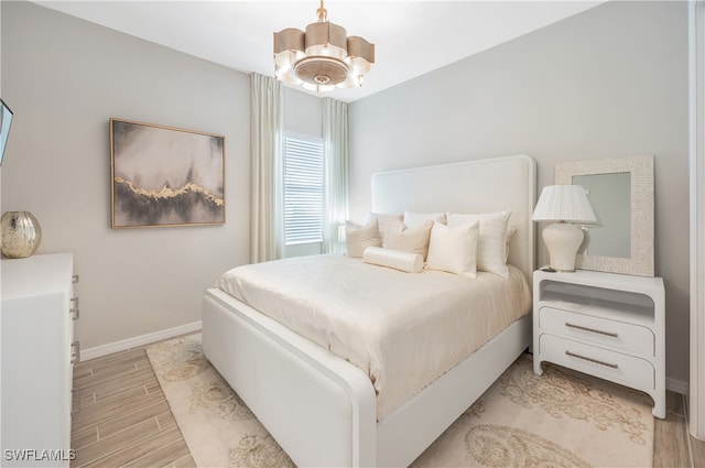 bedroom with ceiling fan with notable chandelier and light hardwood / wood-style flooring