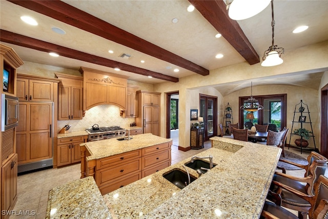 kitchen featuring a large island with sink, a kitchen breakfast bar, light stone countertops, beamed ceiling, and decorative light fixtures