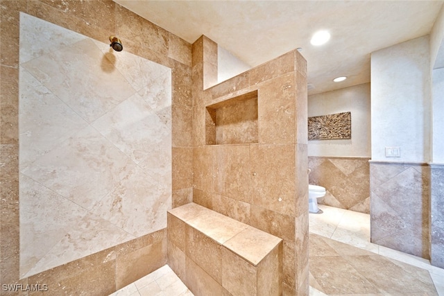 bathroom with a tile shower, toilet, and tile walls