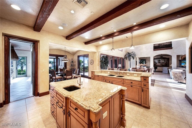 kitchen with sink, hanging light fixtures, beamed ceiling, a large island, and light stone counters