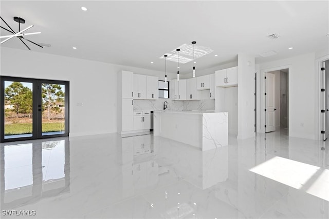 interior space featuring white cabinetry, french doors, a center island, a chandelier, and decorative light fixtures