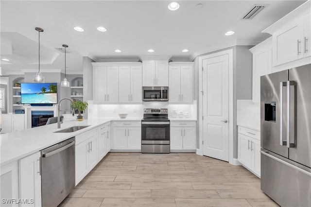 kitchen with white cabinetry, sink, light hardwood / wood-style floors, decorative light fixtures, and appliances with stainless steel finishes