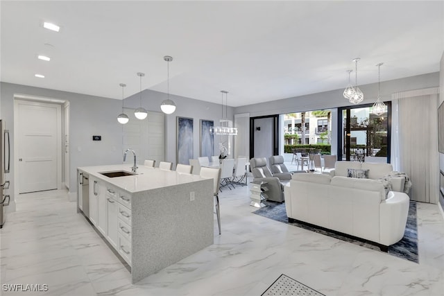 kitchen with pendant lighting, a kitchen island with sink, sink, stainless steel fridge, and white cabinetry