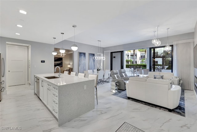 kitchen featuring a kitchen island with sink, sink, white cabinets, stainless steel refrigerator, and hanging light fixtures