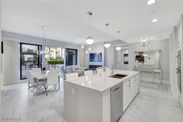 kitchen featuring stainless steel appliances, a kitchen island with sink, sink, pendant lighting, and white cabinetry