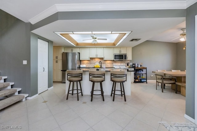 kitchen with crown molding, a raised ceiling, decorative backsplash, appliances with stainless steel finishes, and a ceiling fan