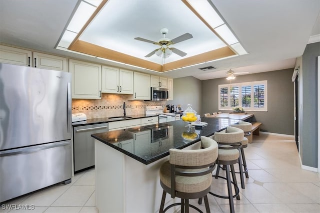 kitchen featuring stainless steel appliances, a sink, visible vents, decorative backsplash, and a raised ceiling