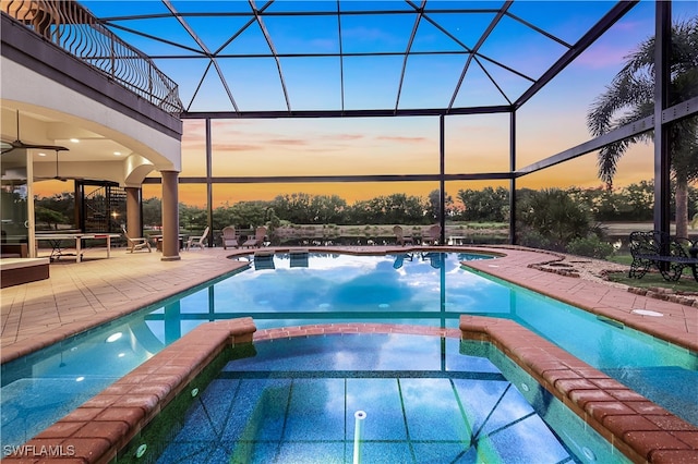 pool at dusk featuring glass enclosure, a patio area, and an in ground hot tub