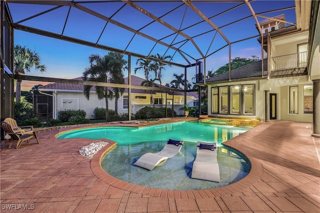 pool at dusk with a patio area, a lanai, and an in ground hot tub